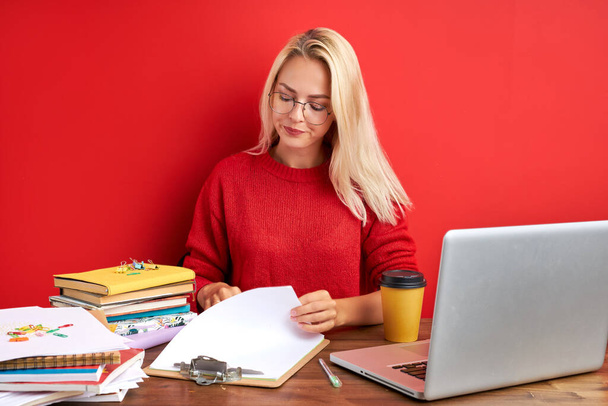 portrait of confident caucasian blonde female sitting at office desk with laptop and papers - Foto, imagen
