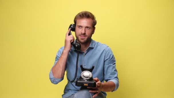 handsome seated businessman holding a telephone on his lap, talking on the phone, arguing, yelling and being angry on yellow background - Footage, Video