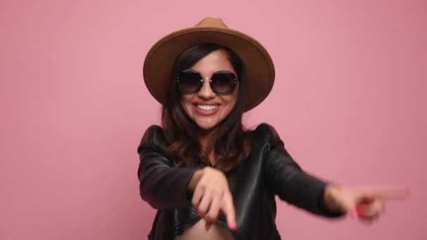 cool girl in leather jacket dancing, waving, smiling and having good time, pointing fingers, sticking out tongue, making thumbs up sign, holding fsts in the air and celebrating on pink background - Кадры, видео