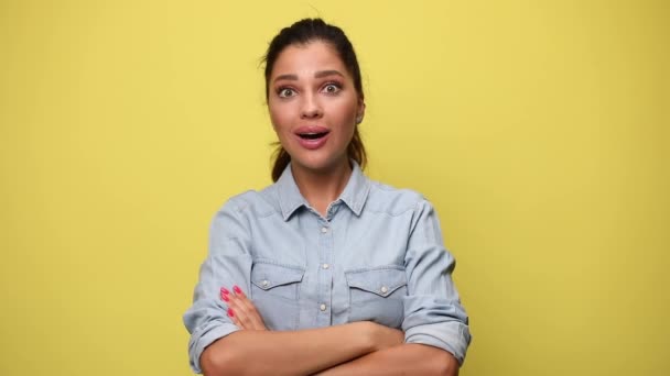 surprised casual girl in blue denim shirt hearing good news, opening mouth and touching head, holding fists in the air, dancing and celebrating on yellow background - Footage, Video