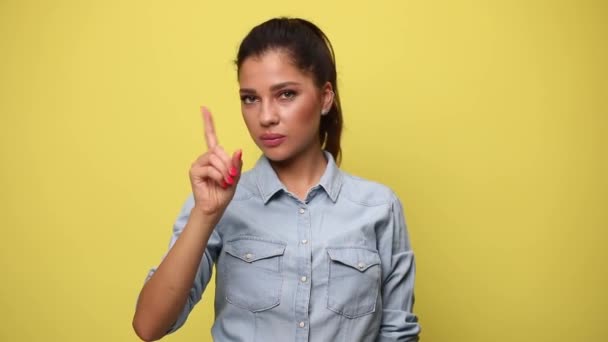 giovane donna casual in camicia di jeans blu facendo un gesto di avvertimento, annuendo in modo negativo e negando su sfondo giallo - Filmati, video