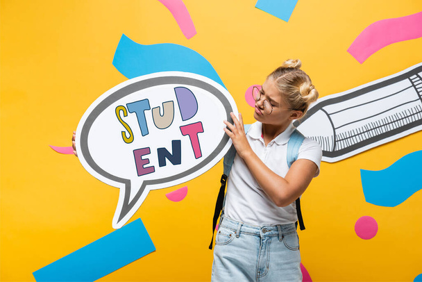 estudante cético segurando bolha de fala com estudante lettering perto de lápis de papel e elementos abstratos em amarelo - Foto, Imagem