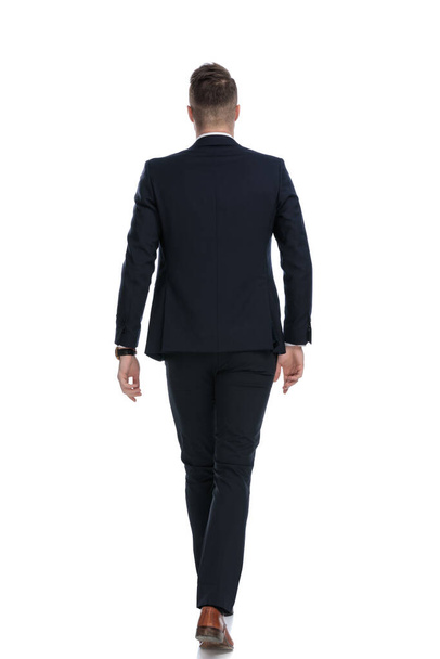 Rear view of young businessman wearing suit and walking on white studio background - Fotoğraf, Görsel