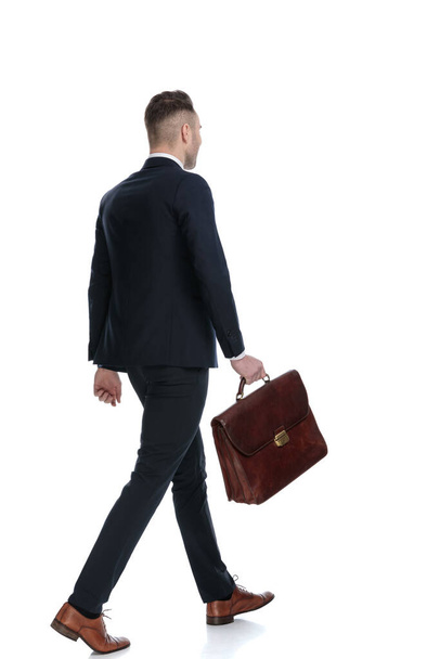 Side rear view of businessman holding briefcase and walking on white studio background - Photo, Image
