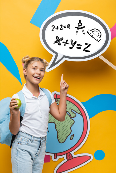 Schulkind mit Rucksack und Apfel zeigt auf Papier-Sprechblase mit mathematischer Formel-Illustration auf gelbem Hintergrund - Foto, Bild