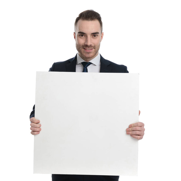 Positive businessman holding blank billboard and smiling while standing on white studio background - Foto, Imagem