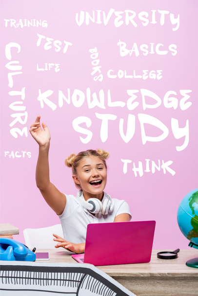Studentessa seduta con mano alzata vicino a laptop, telefono, lettering e arte cartacea su rosa  - Foto, immagini