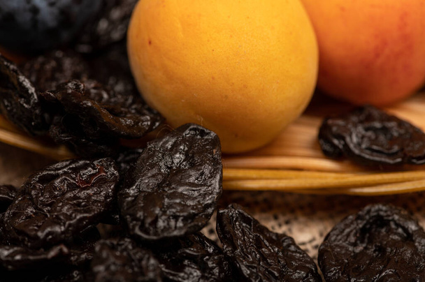 Ripe apricots, juicy black plums and dried prunes in a wicker basket. Close up. Autumn harvest - 写真・画像