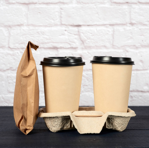 two brown paper disposable cups with a plastic lid stand in the tray, white background, takeaway containers - Photo, Image