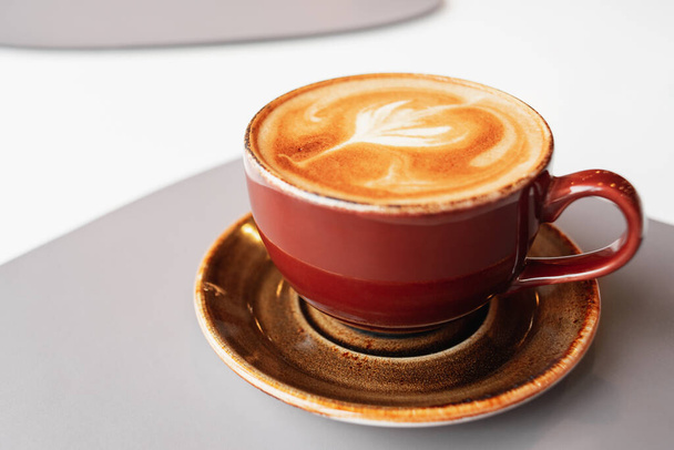 Café de la mañana en una taza de cerámica con espuma en un platillo. Pausa para el café en un café. Aroma capuchino fresco. Taza de café en la mesa. - Foto, imagen