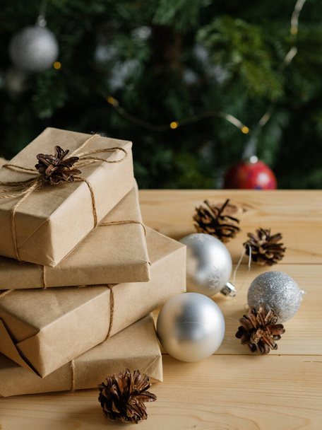 Vánoční dárky v řemeslném balení na dřevěném stole na pozadí zdobeného vánočního stromečku. Koncept Vánoc a Nového roku. - Fotografie, Obrázek