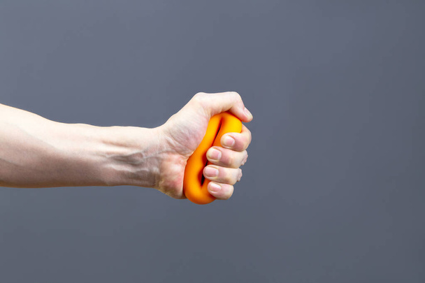 Man squeezing an orange rubber grip exerciser isolated on grey background, hand closeup. Sport and fitness concept - Photo, Image
