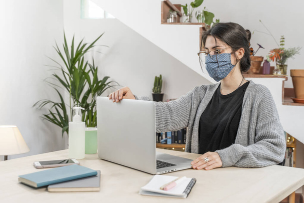 Coronavirus. Young business woman isolated working from home wearing protective mask. Woman in quarantine for coronavirus wearing home made mask. Working from home with sanitizer gel. Quarantine.  - Photo, image