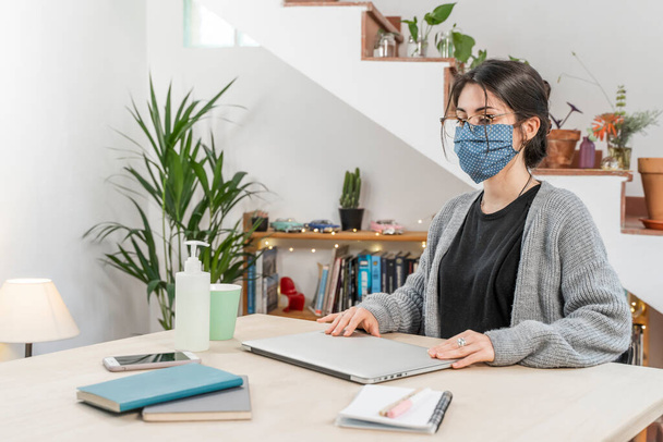 Coronavirus. Young business woman isolated working from home wearing protective mask. Woman in quarantine for coronavirus wearing home made mask. Working from home with sanitizer gel. Quarantine.  - Zdjęcie, obraz