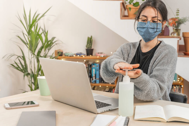 Coronavirus. Young business woman isolated working from home wearing home made protective mask. Woman in quarantine for coronavirus using sanitizer gel meanwhile she is working. Quarantine.  - Foto, Bild