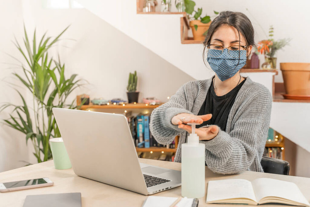 Coronavirus. Young business woman isolated working from home wearing home made protective mask. Woman in quarantine for coronavirus using sanitizer gel meanwhile she is working. Quarantine.  - Φωτογραφία, εικόνα