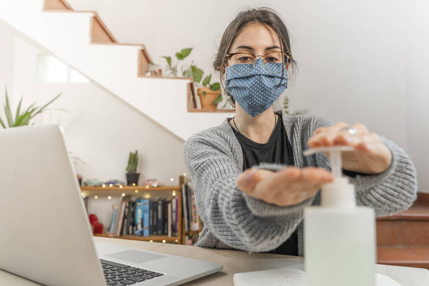 Coronavirus. Young business woman isolated working from home wearing home made protective mask. Woman in quarantine for coronavirus using sanitizer gel meanwhile she is working. Quarantine.  - Photo, image