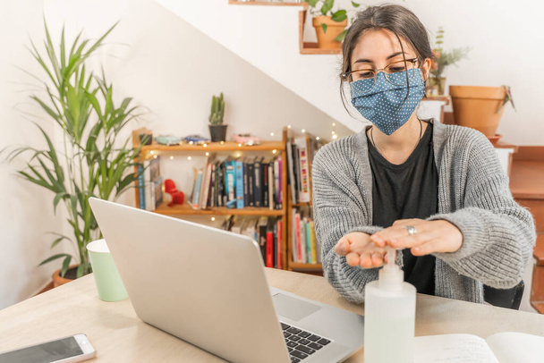 Coronavirus. Young business woman isolated working from home wearing home made protective mask. Woman in quarantine for coronavirus using sanitizer gel meanwhile she is working. Quarantine.  - Photo, Image
