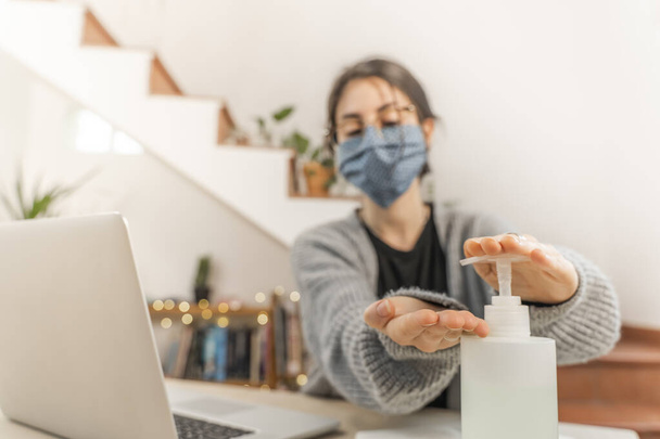 Coronavirus. Young business woman isolated working from home wearing home made protective mask. Woman in quarantine for coronavirus using sanitizer gel meanwhile she is working. Quarantine.  - Foto, imagen