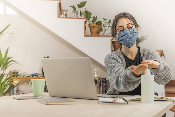Coronavirus. Young business woman isolated working from home wearing home made protective mask. Woman in quarantine for coronavirus using sanitizer gel meanwhile she is working. Quarantine.  - Photo, image