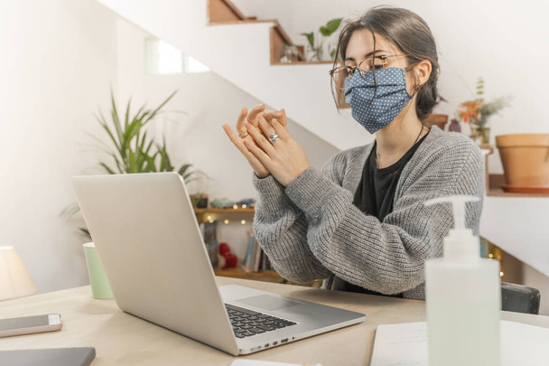 Coronavirus. Young business woman isolated working from home wearing home made protective mask. Woman in quarantine for coronavirus using sanitizer gel meanwhile she is working. Quarantine.  - Zdjęcie, obraz