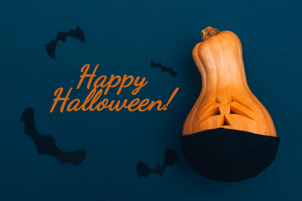 Halloween pumpkin in black protective medical mask,bats from black paper on dark blue background.Inscription HAPPY HALLOWEEN! on an dark background.Halloween and covid-19 concept. - Fotografie, Obrázek