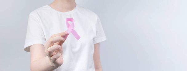 World Breast cancer day concept. Woman in white T-shirt holds pink ribbon in her hand. October Breast Cancer Awareness month. Copy space - 写真・画像