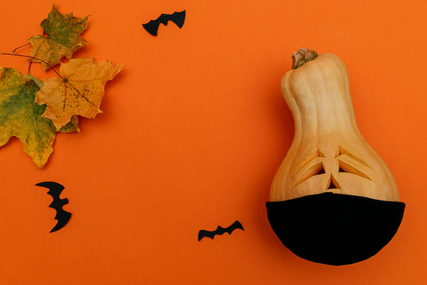 Halloween pumpkin in black protective medical mask,bats from black paper and maple leaf on orange background.Halloween and covid-19 concept.Copy space,top view - Fotoğraf, Görsel
