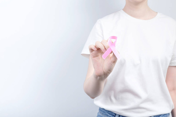 World Breast cancer day concept. Woman in white T-shirt holds pink ribbon in her hand. October Breast Cancer Awareness month. Copy space - Foto, Imagen