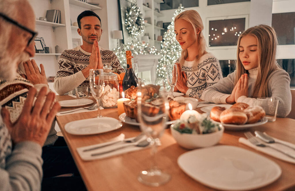 The beautiful family sitting at the christmas table and praying - Photo, Image