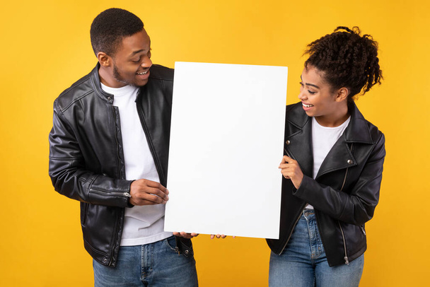 Africký pár ukazuje prázdný plakát s prázdným prostorem, žluté pozadí - Fotografie, Obrázek