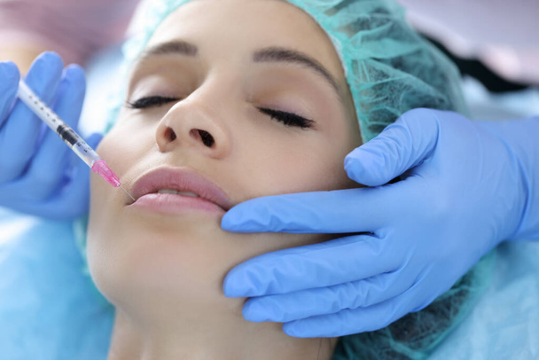 Kosmetikerin in Gummihandschuhen spritzt junge Frau Kollagen in die Lippen - Foto, Bild