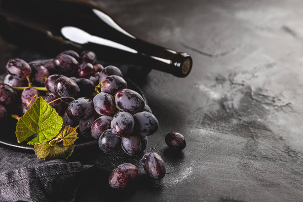 Purple grapes on a plate and wine bottle on a dark background with copy space - Zdjęcie, obraz