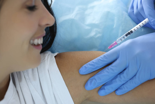 Médecin en gants de caoutchouc injecte la médecine dans l'épaule de la jeune femme - Photo, image