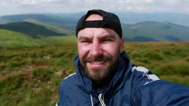 tourism, mountains, lifestyle, nature, people, Selfie concept - Young Man Traveler Makes Selfie On Background Mountains In Summer, at sunset. bearded tourist smiling. slow motion, technology - Video, Çekim