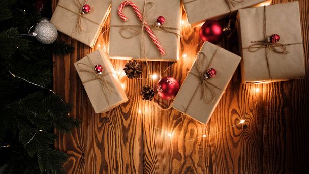 Новорічні або різдвяні подарунки, загорнуті в крафт-папір і прикрашені різдвяними цукерками та іграшками з червоної ялинки на дерев'яному тлі. Різдвяний фон. З Новим роком
 - Фото, зображення