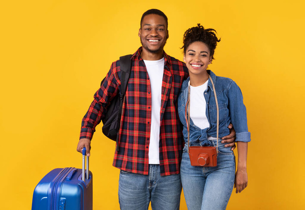 Ευτυχισμένοι μαύροι ταξιδιώτες με βαλίτσα στέκεται πάνω από κίτρινο φόντο - Φωτογραφία, εικόνα