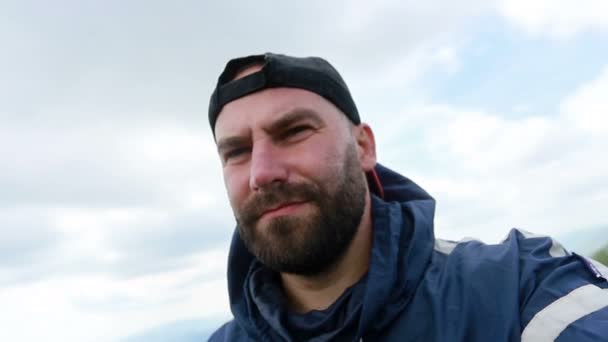 tourism, mountains, lifestyle, nature, people, Selfie concept - Young Man Traveler Makes Selfie On Background Mountains In Summer, at sunset. bearded tourist smiling. slow motion, technology - Filmati, video
