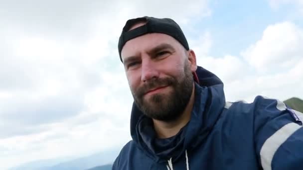 tourism, mountains, lifestyle, nature, people, Selfie concept - Young Man Traveler Makes Selfie On Background Mountains In Summer, at sunset. bearded tourist smiling. slow motion, technology - Materiał filmowy, wideo