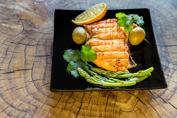 Grilled salmon with lemon and green asparagus black plate - Fotó, kép