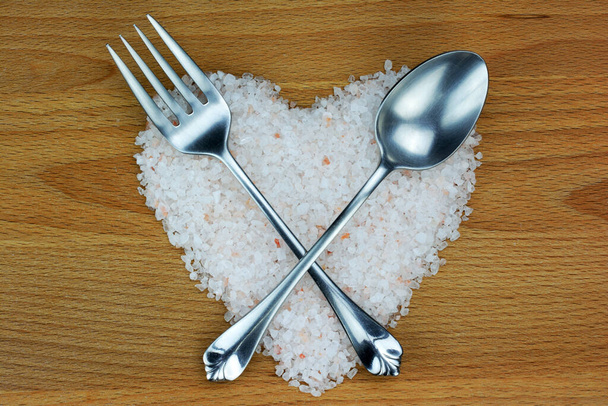 Sól himalajska w kształcie serca ze srebrną łyżeczką i widelcem na drewnianym tle - Zdjęcie, obraz