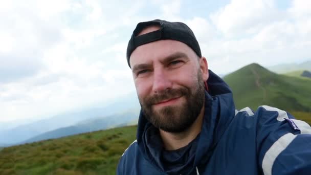 tourism, mountains, lifestyle, nature, people, Selfie concept - Young Man Traveler Makes Selfie On Background Mountains In Summer, at sunset. bearded tourist smiling. slow motion, technology - Séquence, vidéo