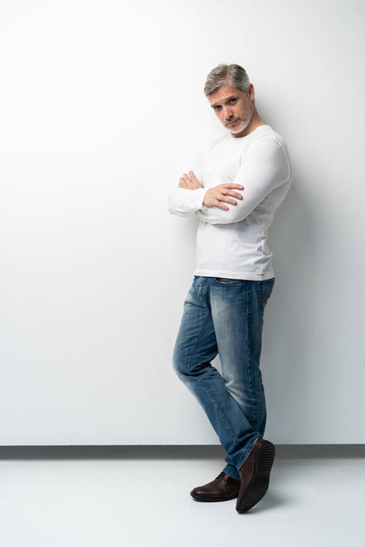 Full body portrait of relaxed mature man standing with arms crossed over white background. - Fotografie, Obrázek