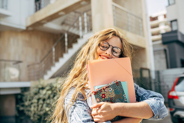 Horizontal image of a pretty college female student carrying lots of books in college campus outside. Beautiful young woman smiling and wearing casual outfit and eyeglasses with books outdoors. - Foto, Bild