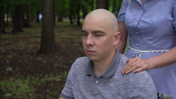 Une femme pose sa main sur l'épaule d'un jeune homme atteint d'un cancer pour le soutenir. L'homme pose sa main sur la main des femmes. Perte de cheveux due à la chimiothérapie. - Photo, image