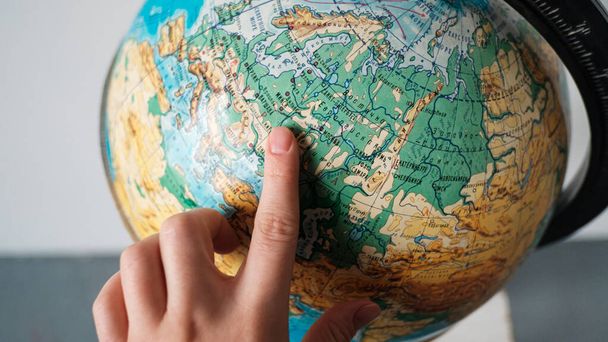 The girl points to a location on the world globe. Chooses a place to travel on the globe. - Fotó, kép