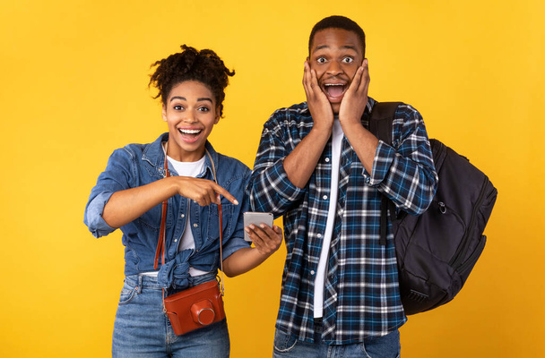 Schwarze Ehepartner zeigen mit dem Finger auf das Handy, gelber Hintergrund - Foto, Bild