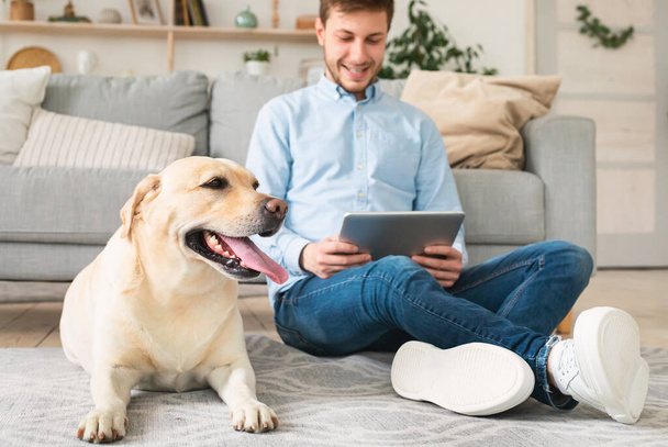 Mann mit digitalem Tablet und Labrador zu Hause - Foto, Bild