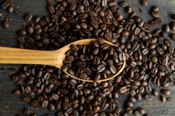 Fresh roasted arabica coffee beans in a wooden spoon and scattered coffee beans on a wooden table. - Foto, Bild