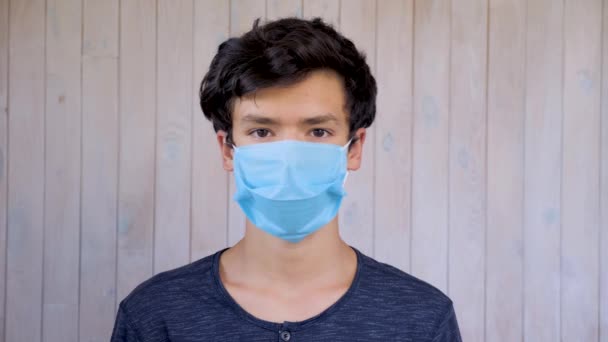 Młody mężczyzna w masce medycznej patrzący w kamerę. Wirus koronawirusowy, epidemia kovidu-19. Brązowe oczy 15-letniego chłopca w masce. Wirus, bakterie, epidemia. Ochrona zdrowia publicznego przed - Materiał filmowy, wideo